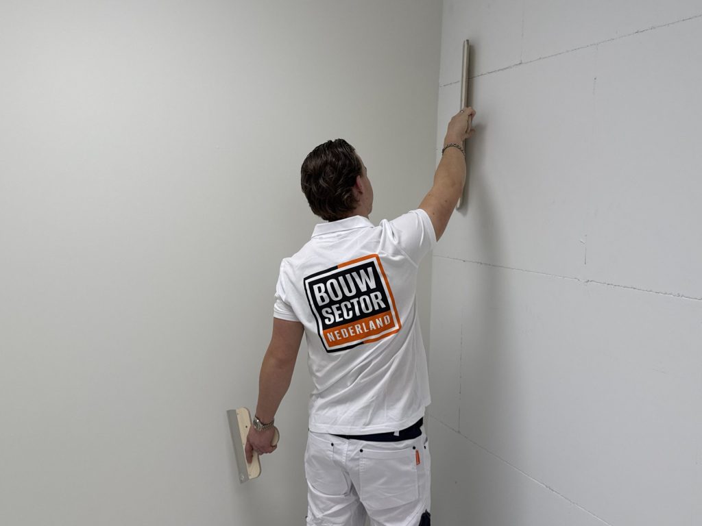 Stukadoor houdt een rei langs de binnenhoek van een kamer om te zien of de wand recht staat