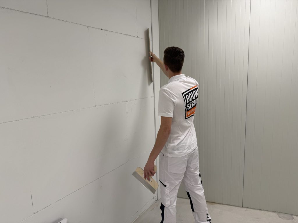 Stukadoor staat schuin voor een lange wand en trekt de pleister met een rei recht langs de hoek