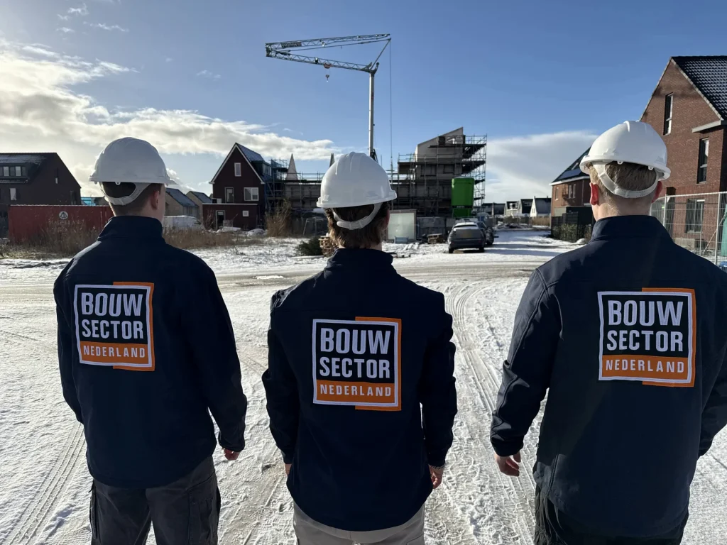 Drie vakmensen van Bouwsector Nederland met helm kijken naar gevels van bakstenen woningen die nog gebouwd worden
