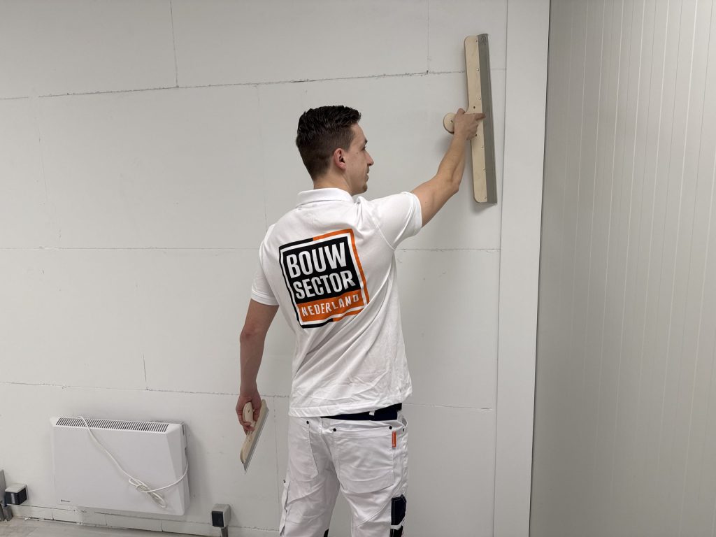 Stukadoor van Bouwsector Nederland trekt met een lange spaan het bovenste deel van een wand vlak