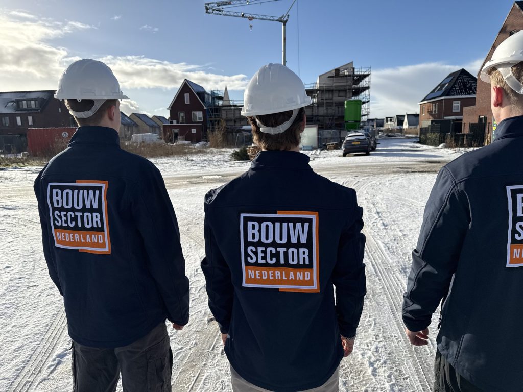 Drie medewerkers van Bouwsector Nederland met witte helm kijken uit over een besneeuwde nieuwbouwstraat met een bouwkraan